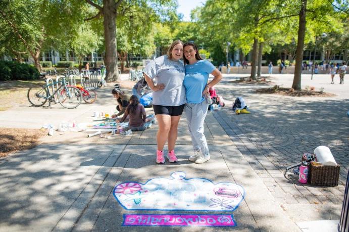 Two students pose for a photo on ODU's campus in front of a crown they painted on the sidewalk. 